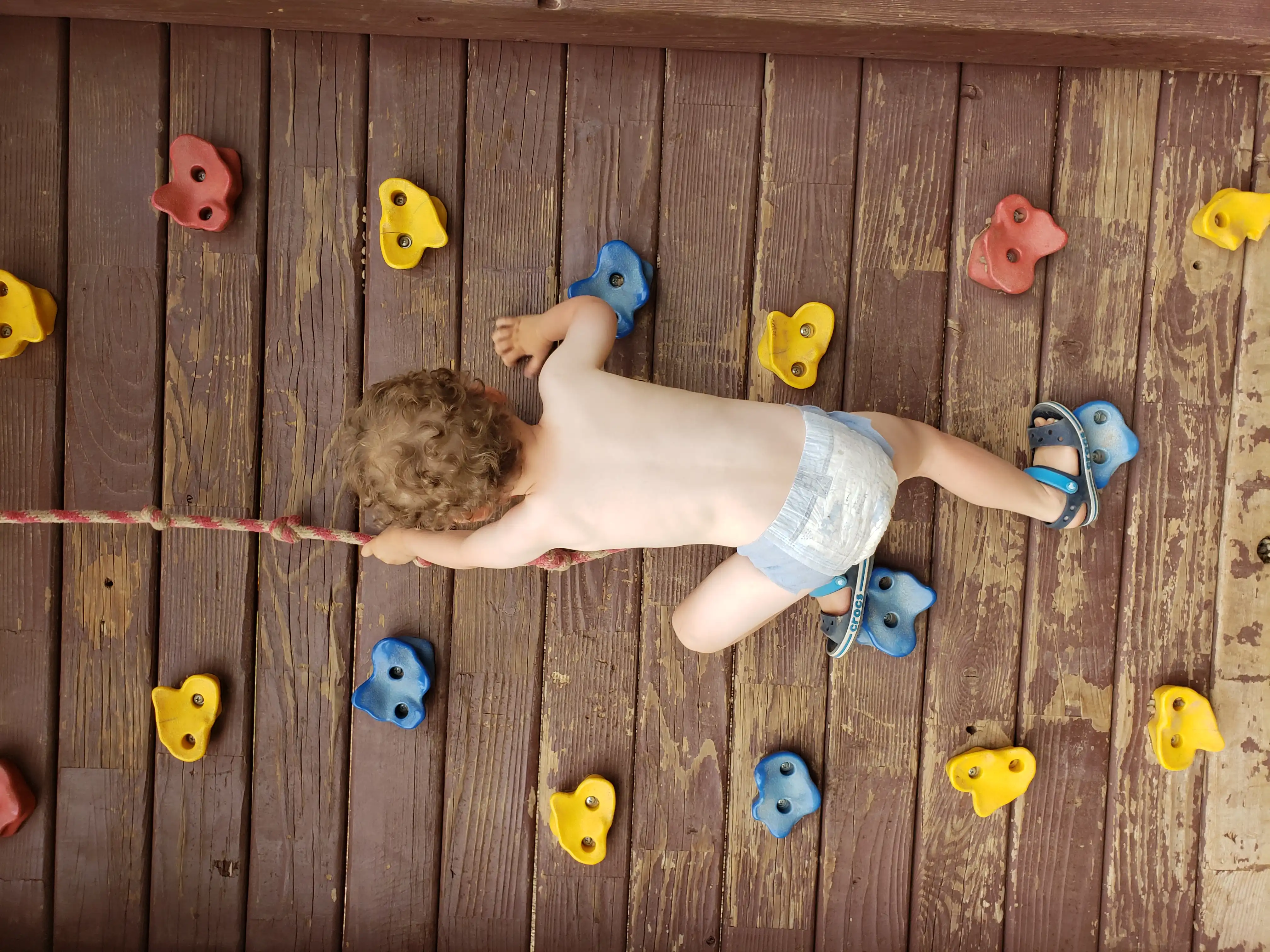 Graham climbing a colorful climbing wall in only his underwear.