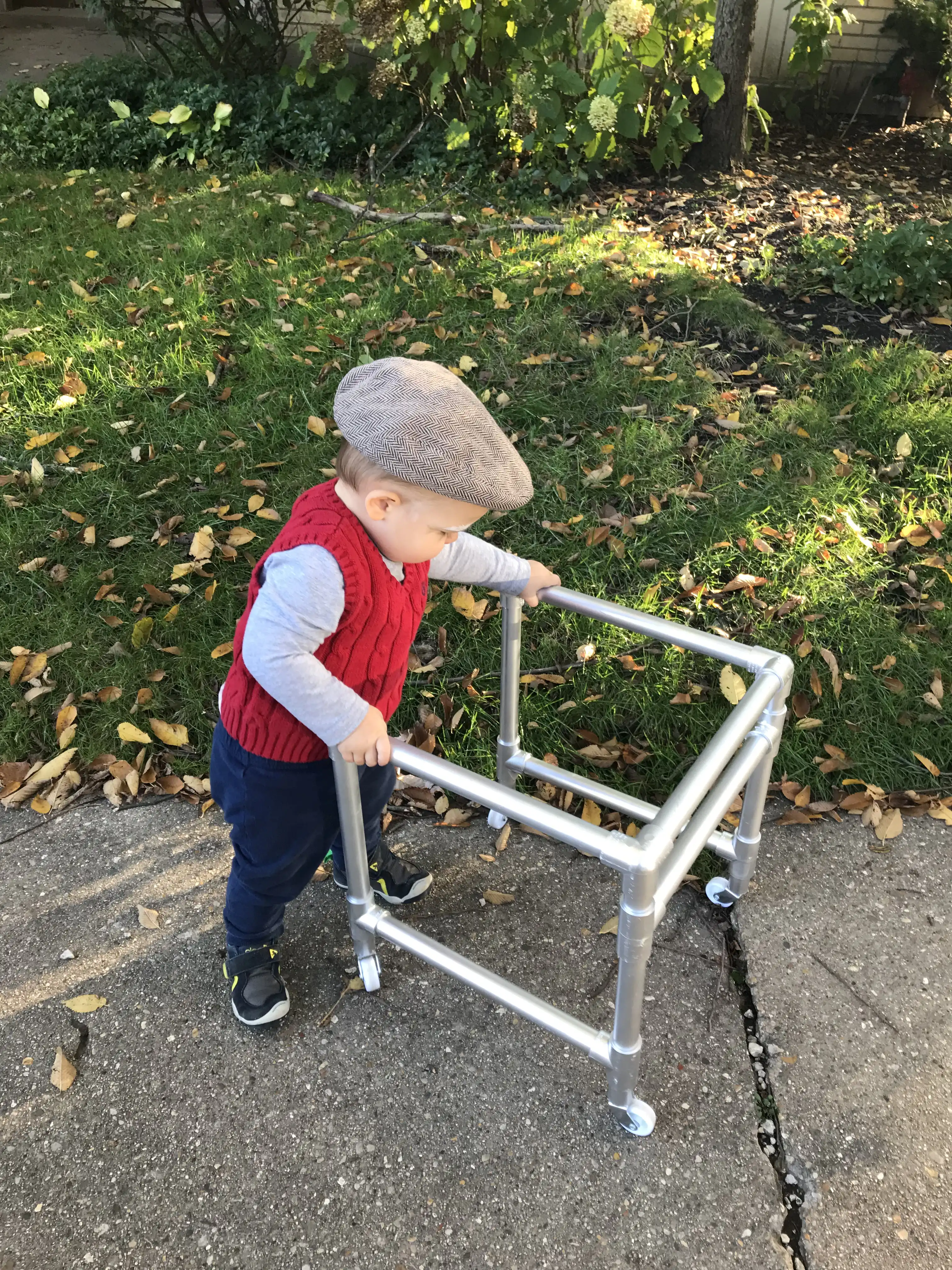 Royal in his old man costume, wearing a red sweater vest, golfer's hat, and pushing a walker