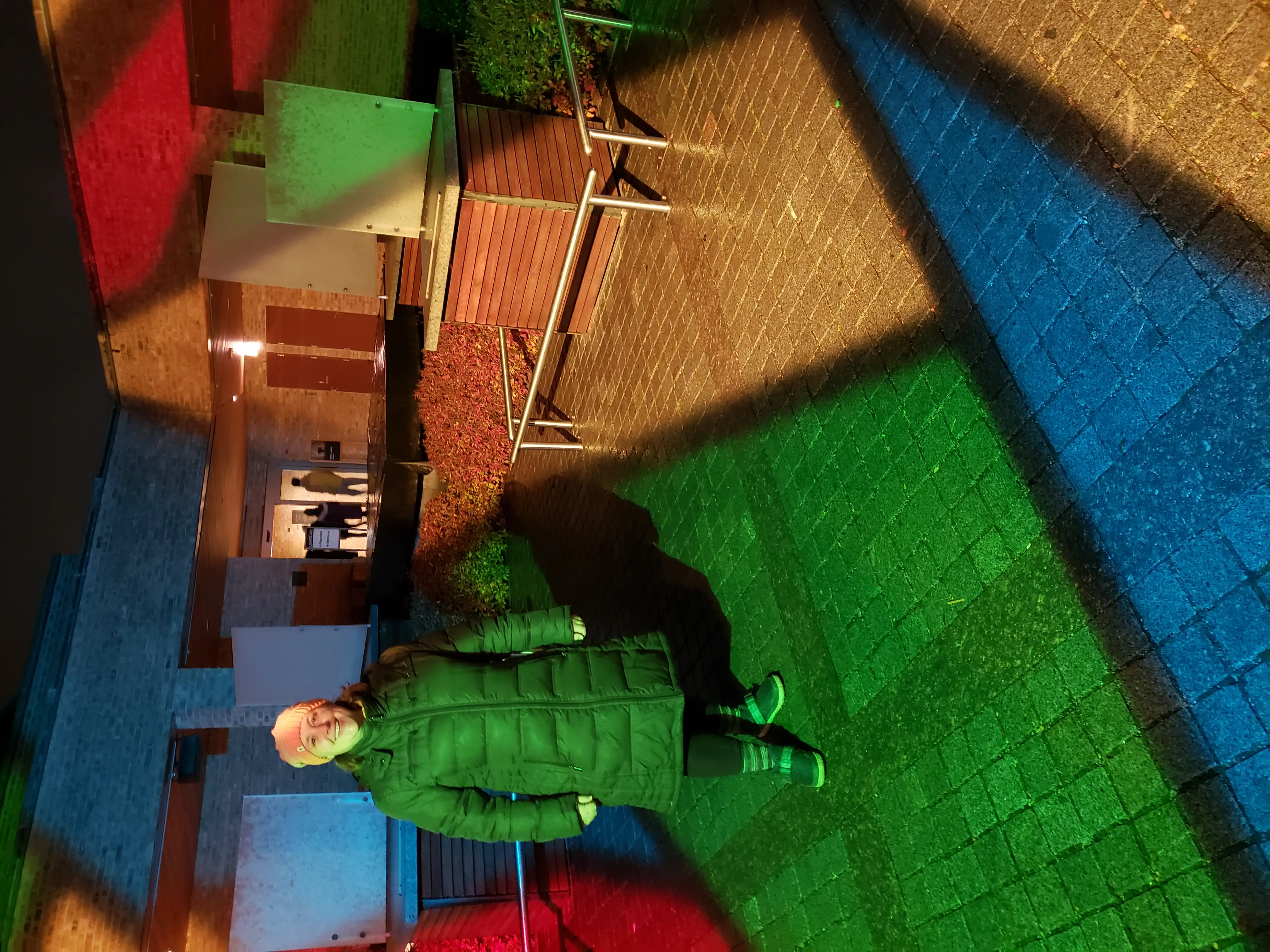 Amie standing in a courtyard colored like a stained glass window from light cast by a many-colored cube.