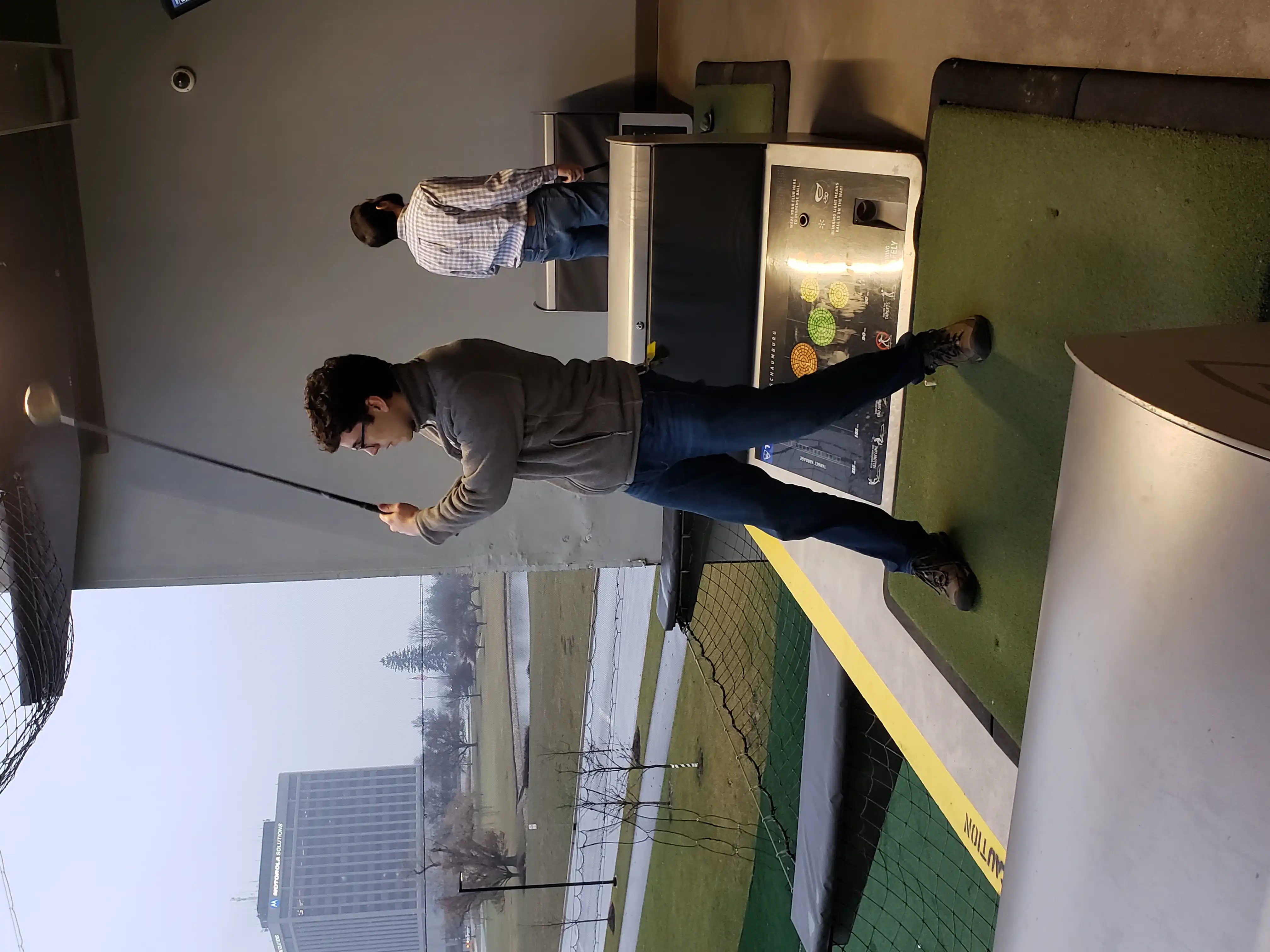 Alex swinging a golf wood from the hitter's box at Top Golf.