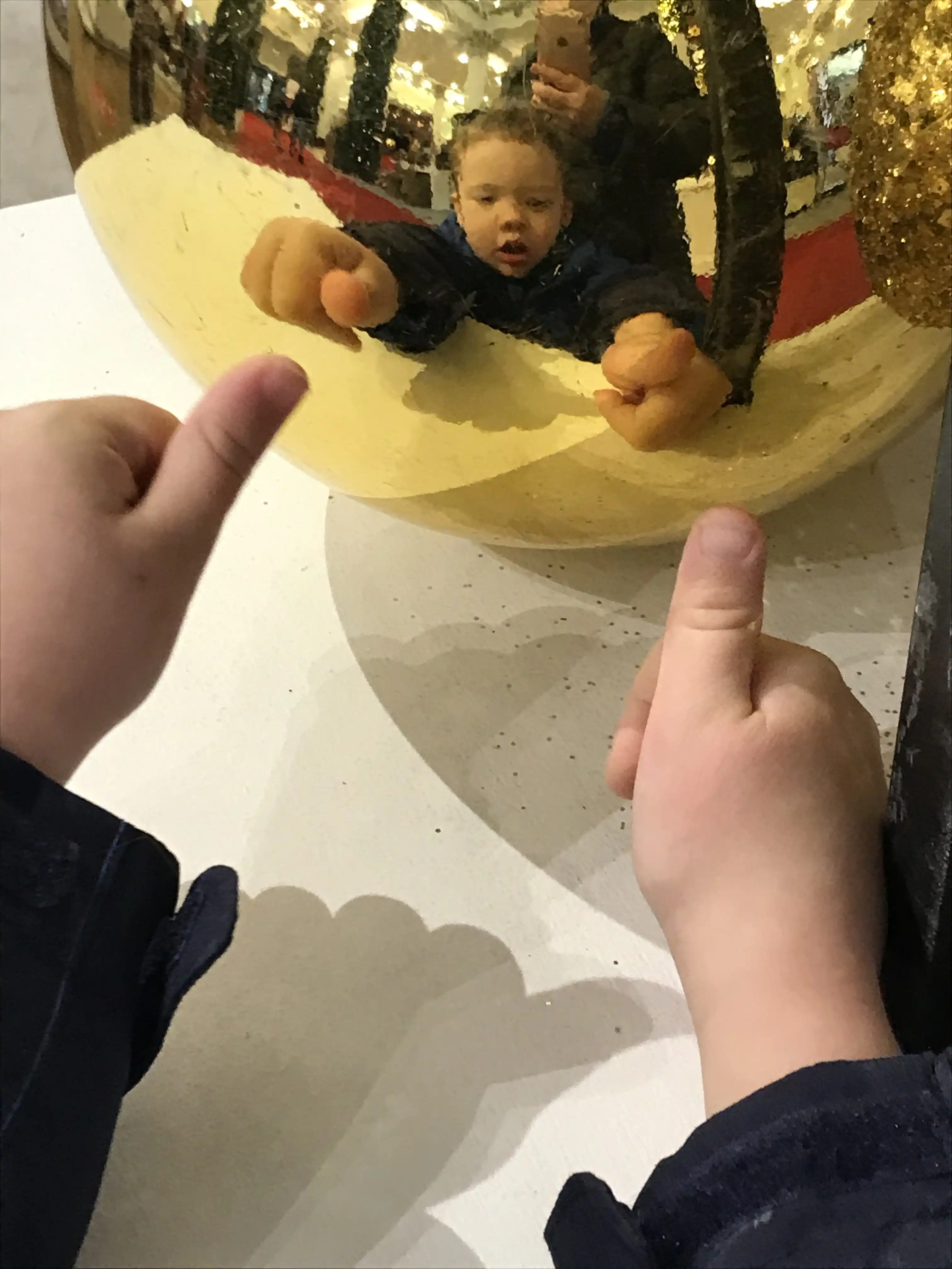 Graham holding up two thumbs up, reflected from a large gold ornament.