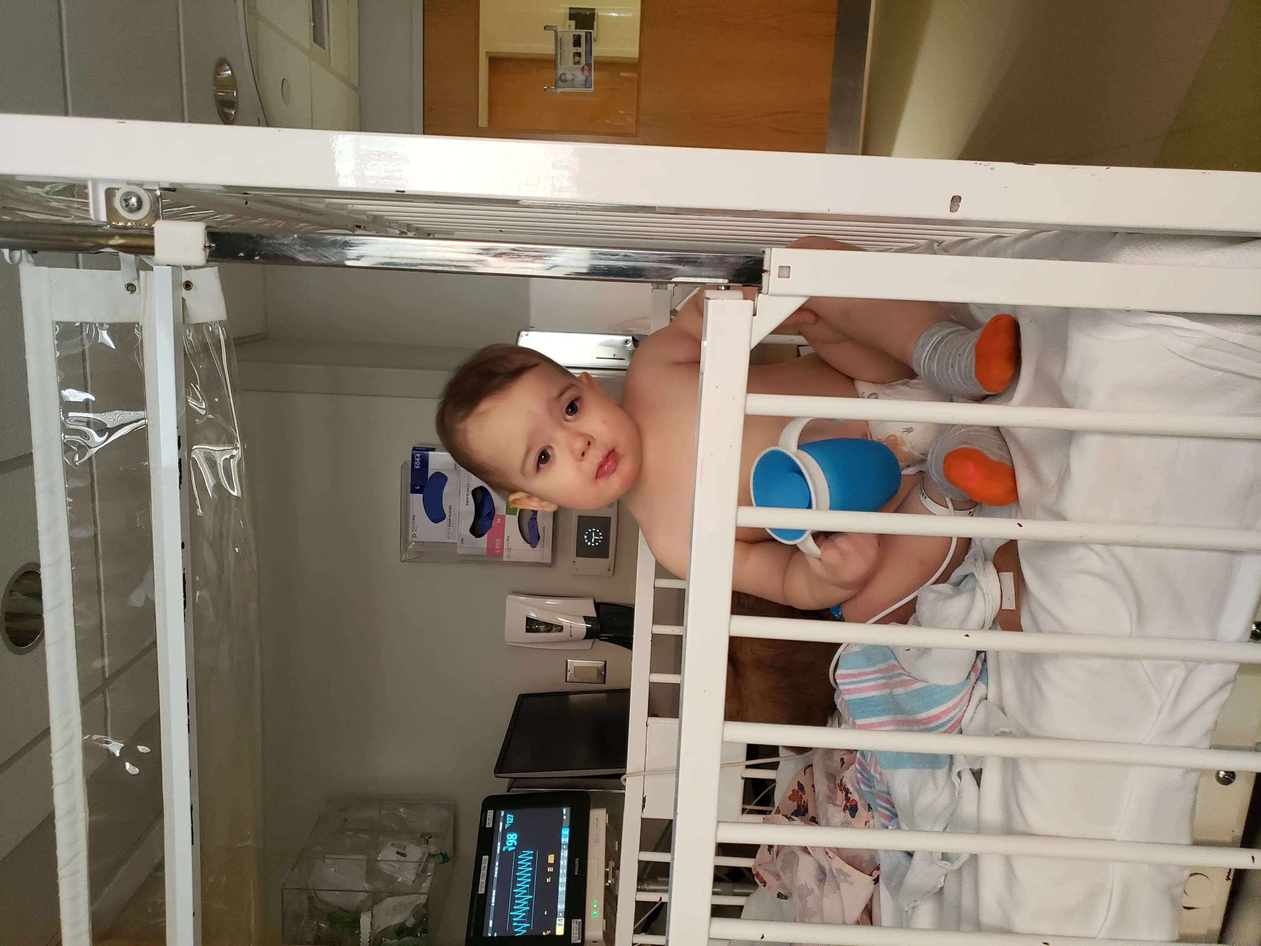 Royal in a hospital room crib, smiling with his head cocked to the left.