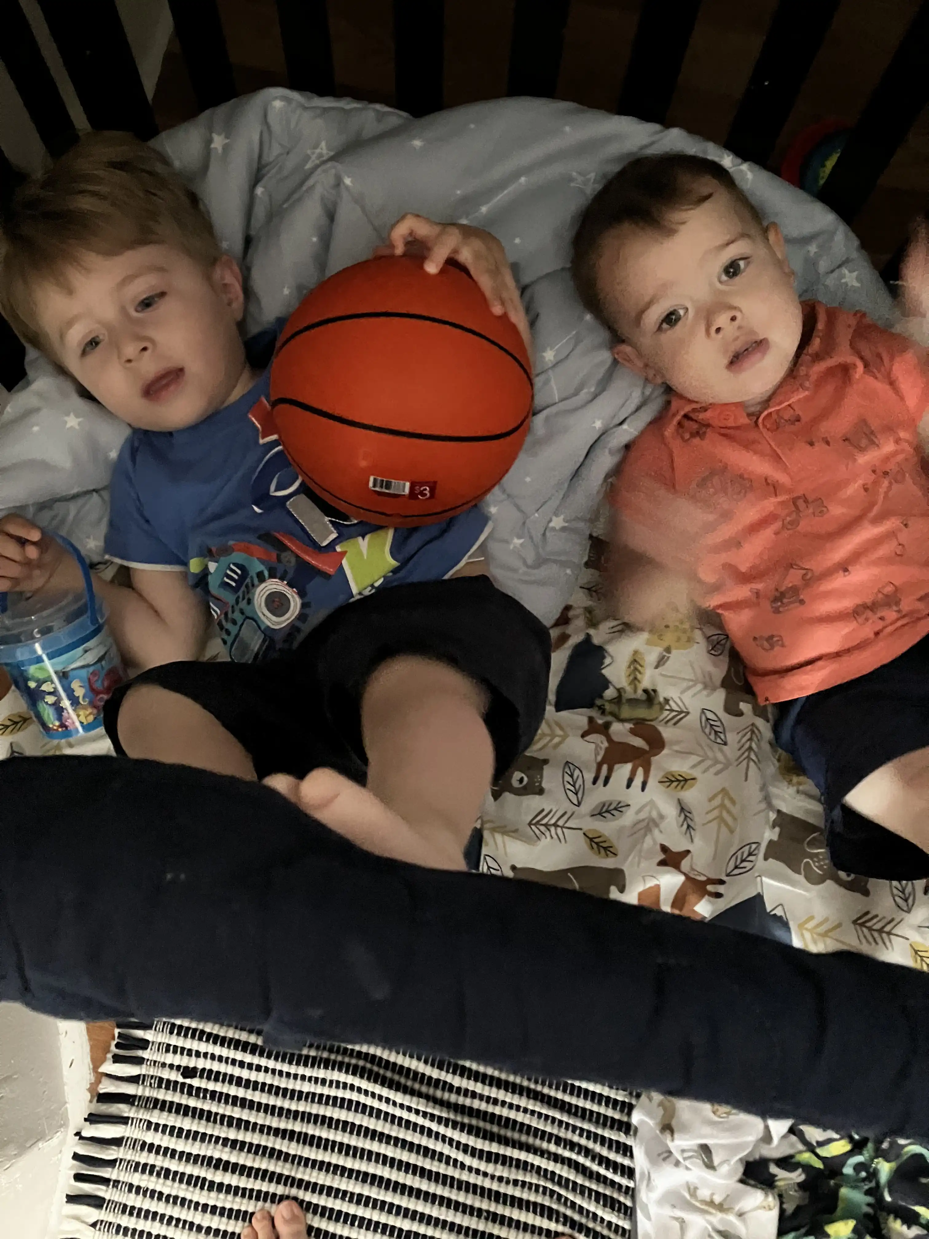 Jotham and Royal laying in a crib with a basketball.