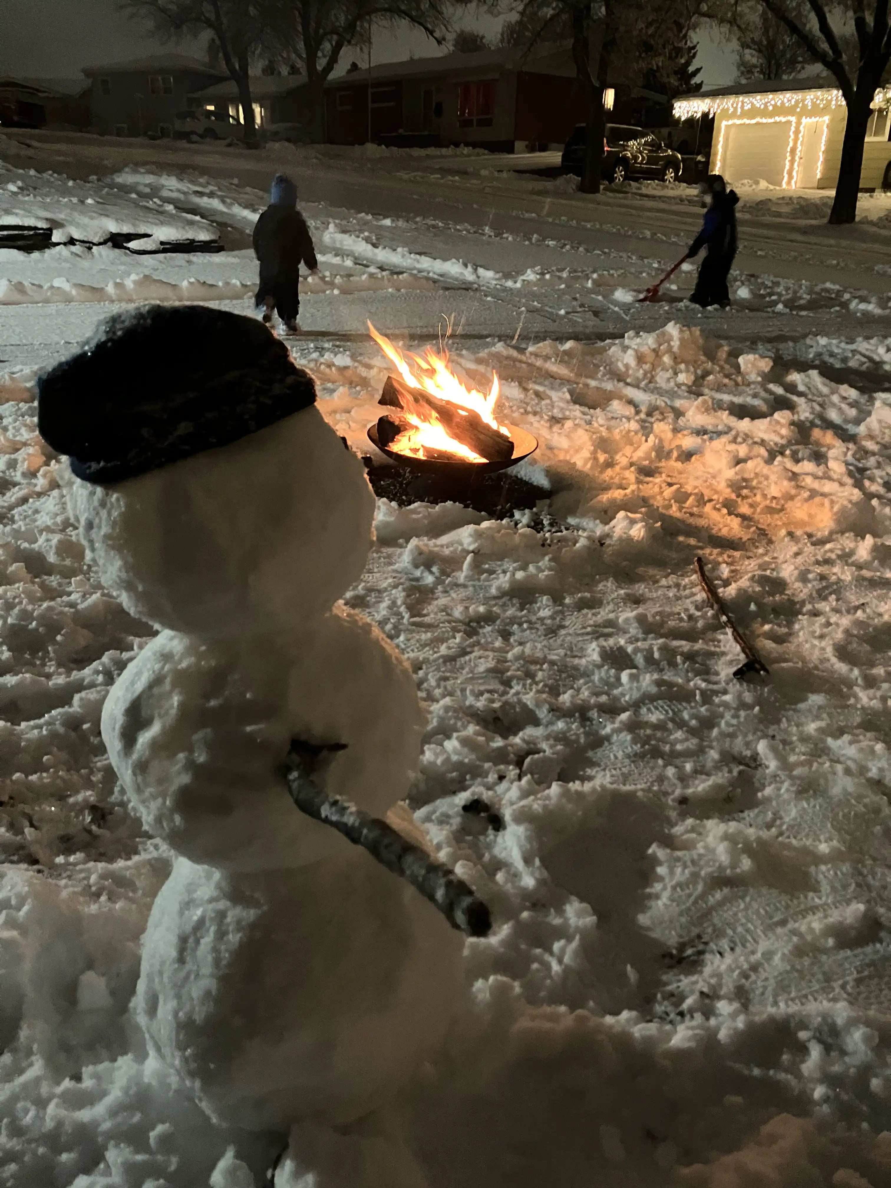 Graham and Royal shoveling the driveway at night while our snowman looks on.