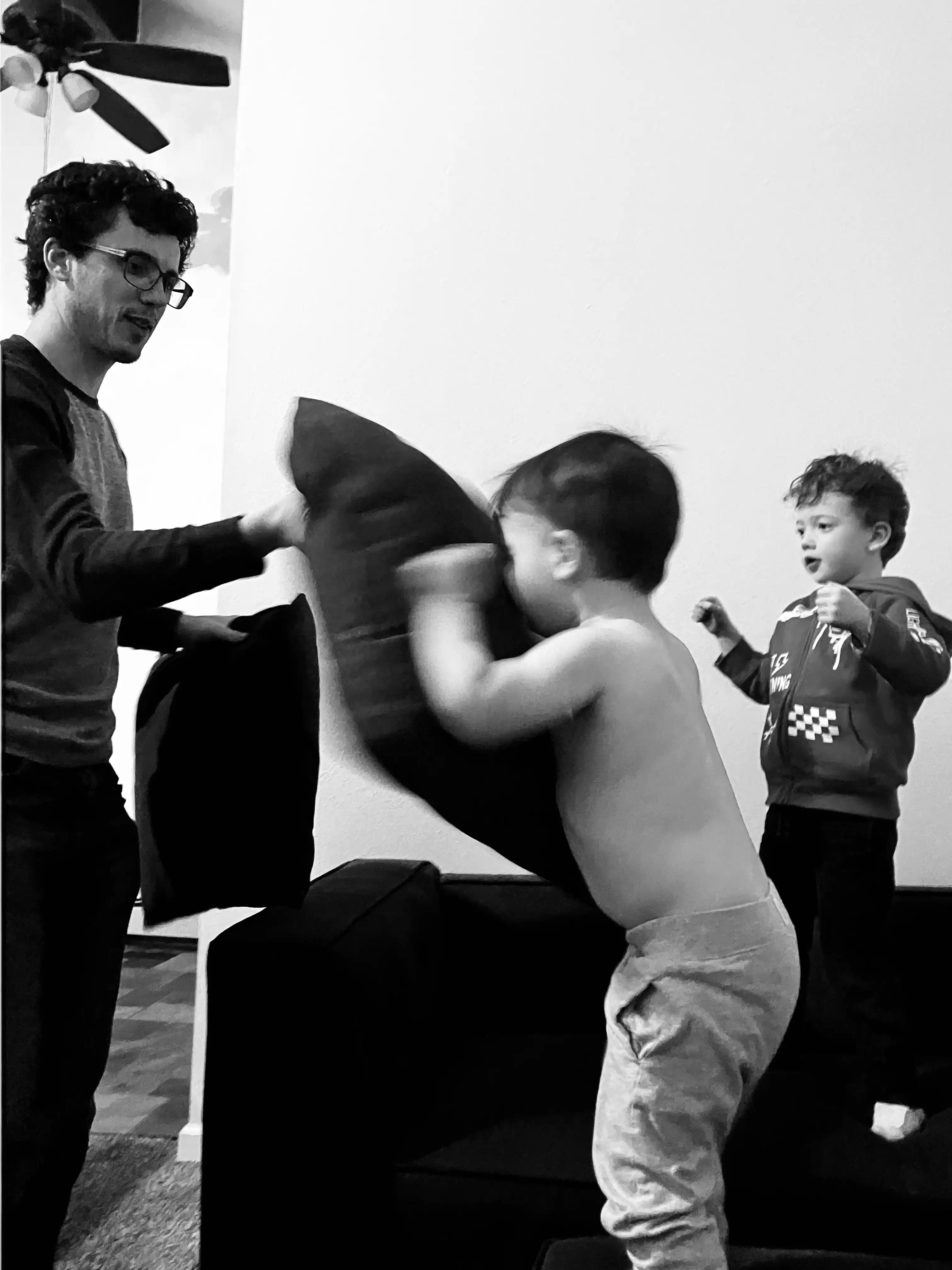 Black and white photo of Alex hitting Royal in the face with a pillow while Graham waits in anticipation.