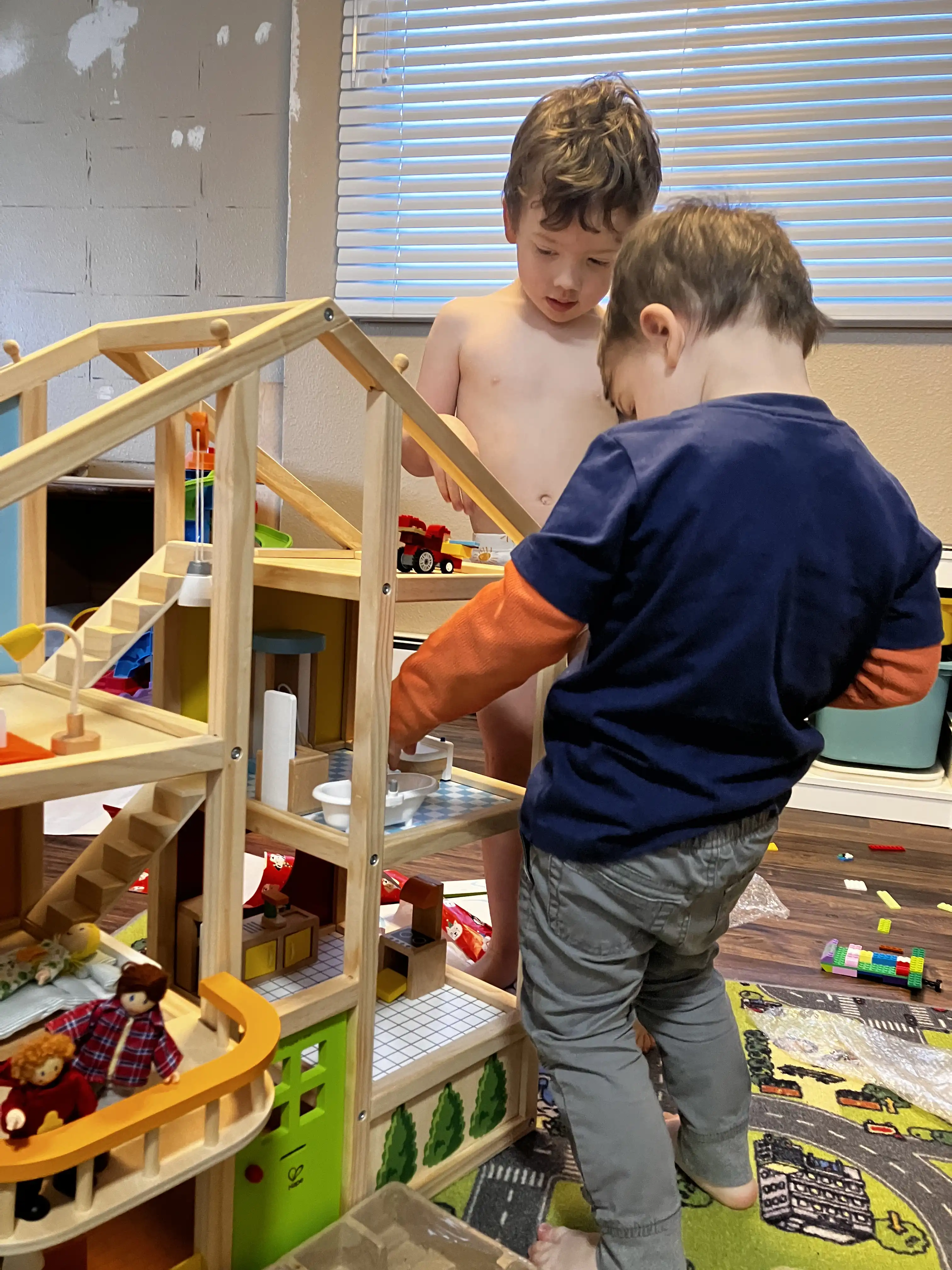 Royal and Graham play with Royal's new wooden dollhouse. Royal is putting one of the dolls into the bathtub, and Graham just placed a lego truck on the third floor.