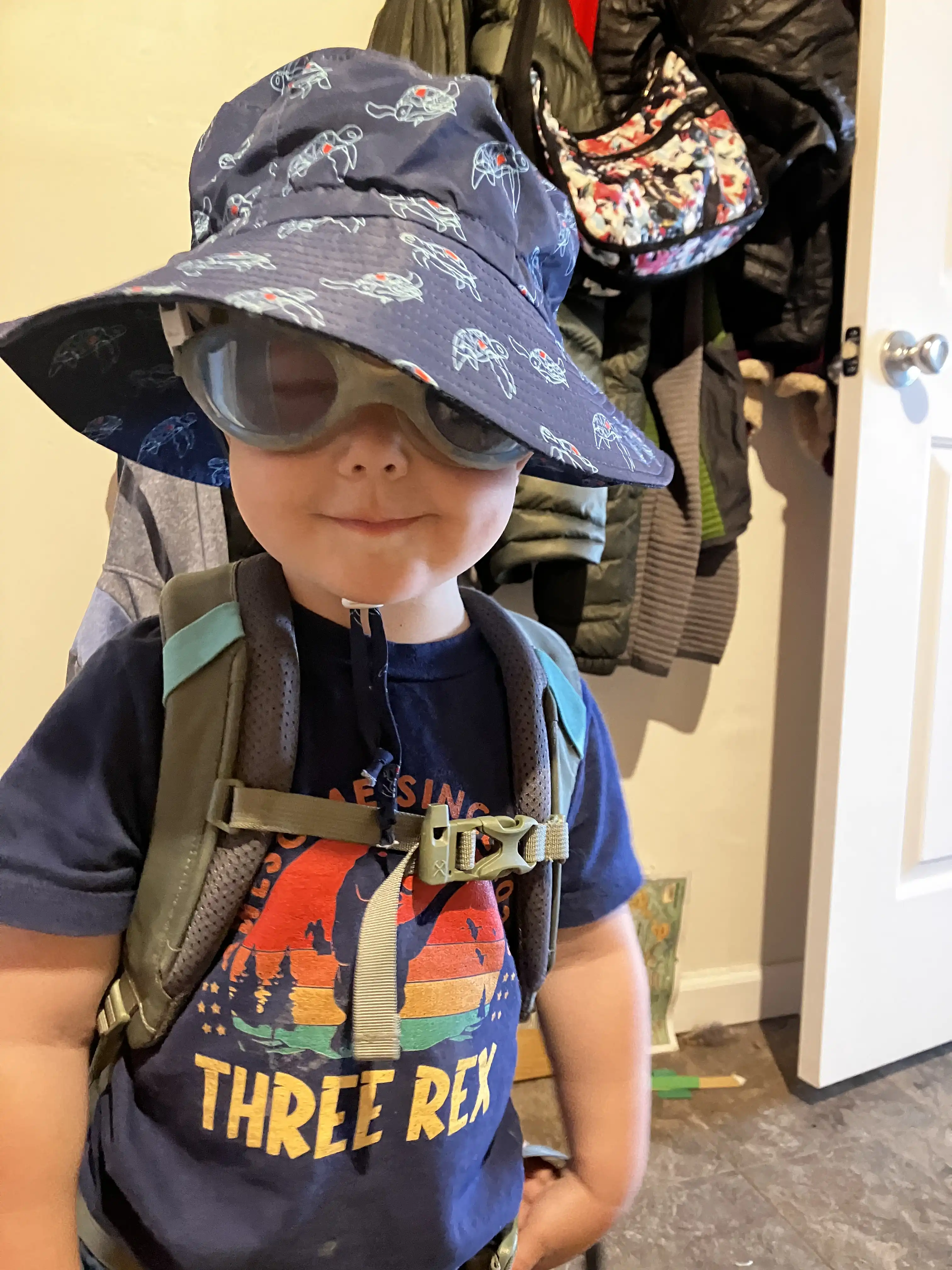 Royal in a boonie hat and blue swim goggles, wearing a grey backpack, ready for a hike.