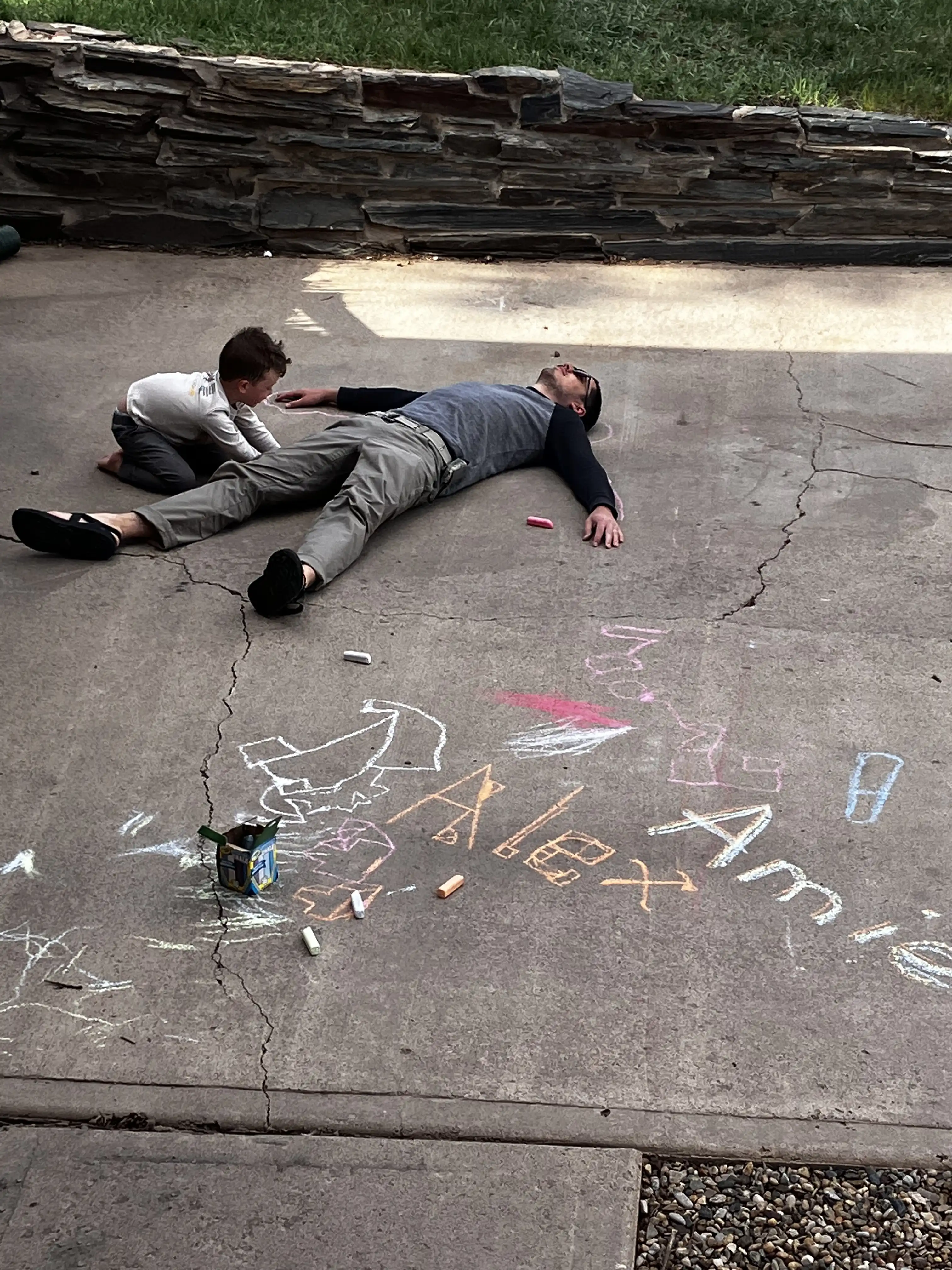 Graham drawing an outline around Alex on the driveway concrete, like a chalk outline of a murder scene.