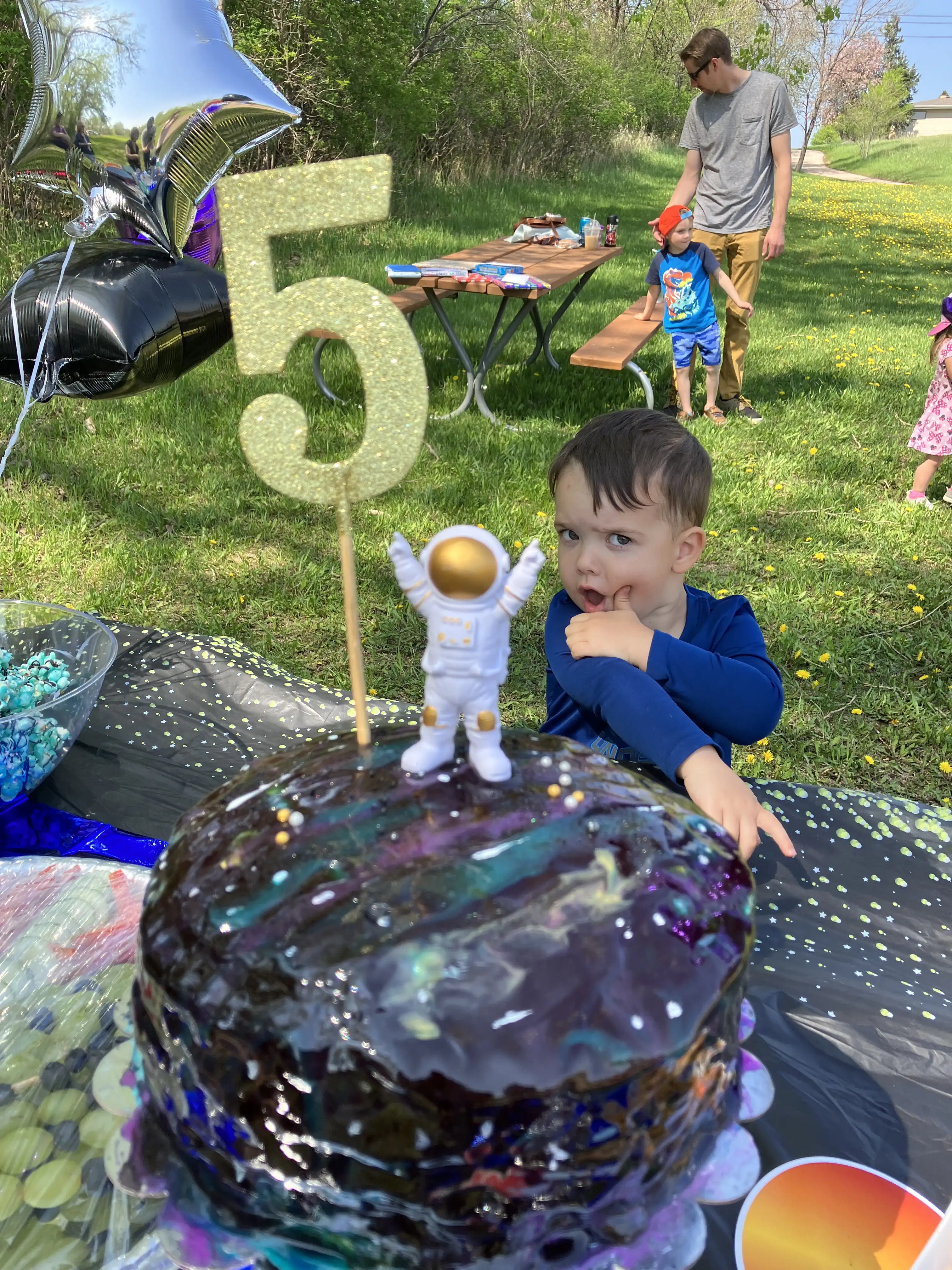 Graham's birthday cake with a golden five and an astronaut on top, with Royal in the background making a funny face.