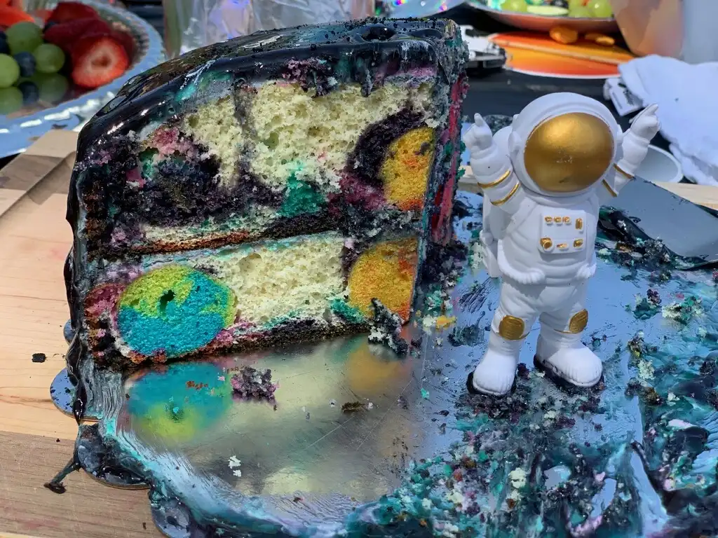 A cross-section of Graham's cake. There's a sun in the middle and planets along the side. The astronaut is placed next to the cake slice.