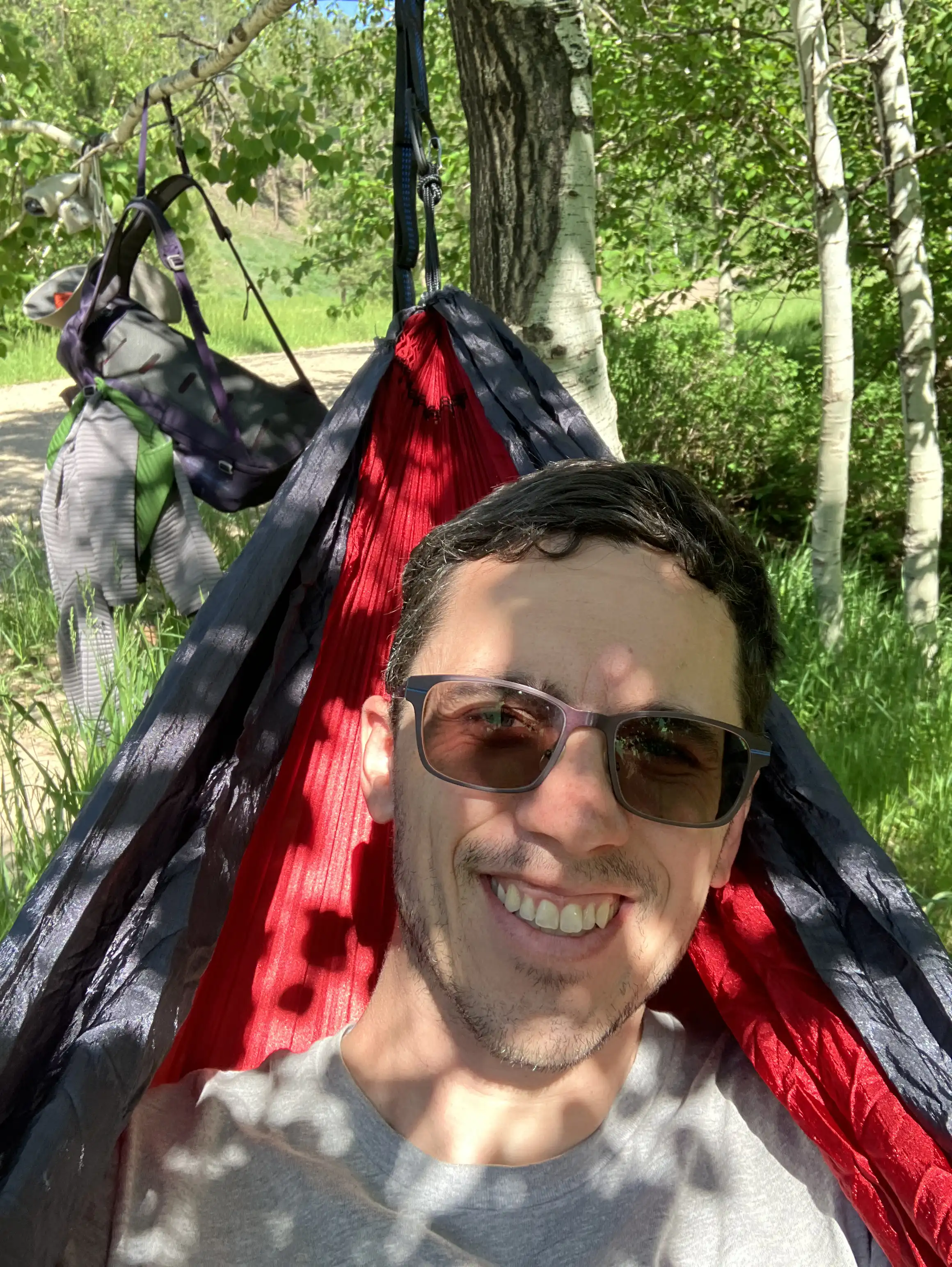 Alex laying in a hammock near Victoria Lake Road with his backpack hanging from a tree in the background