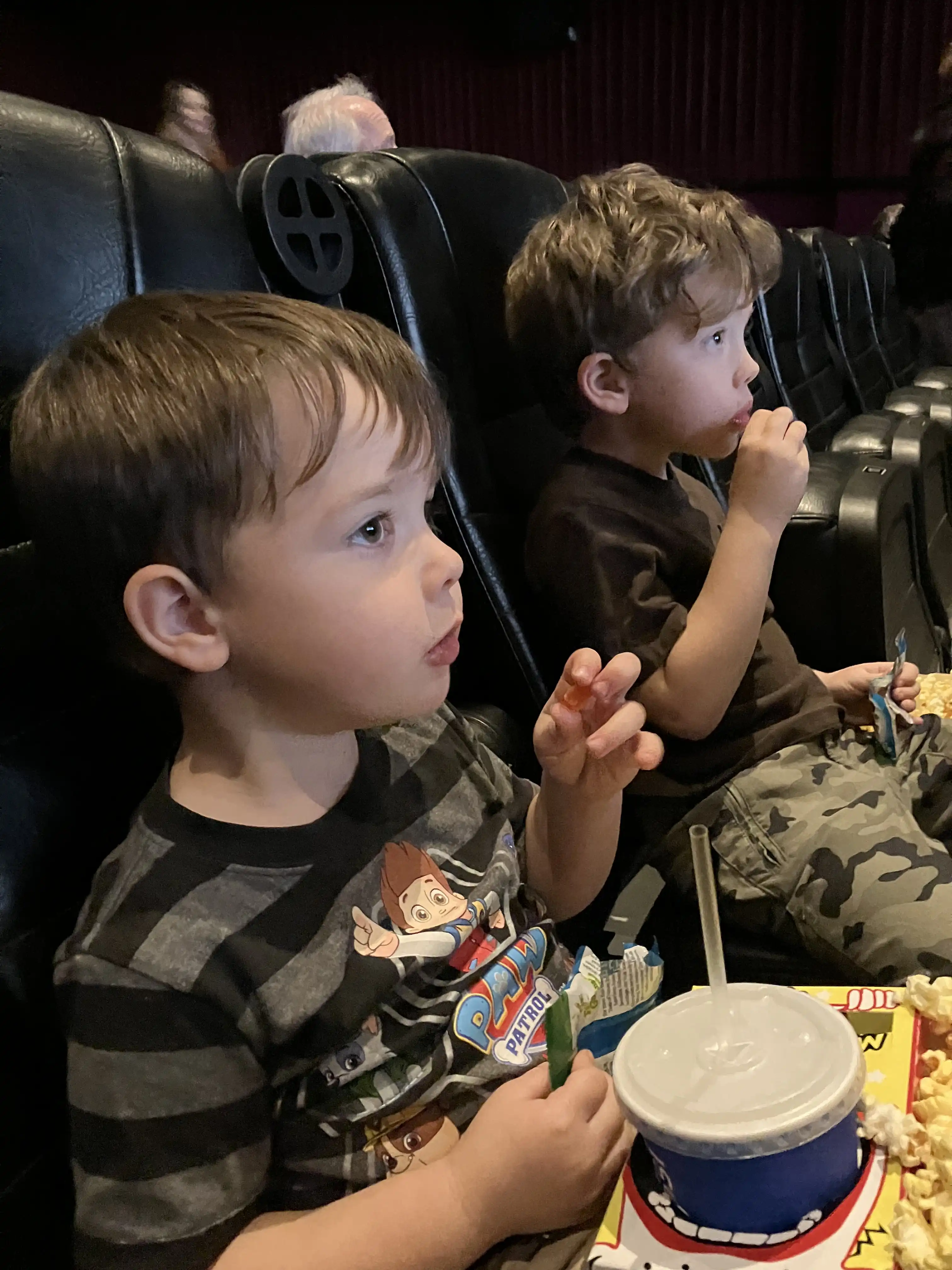 Graham and Royal eating popcorn and drinking water in comfy chairs at the movie theater.