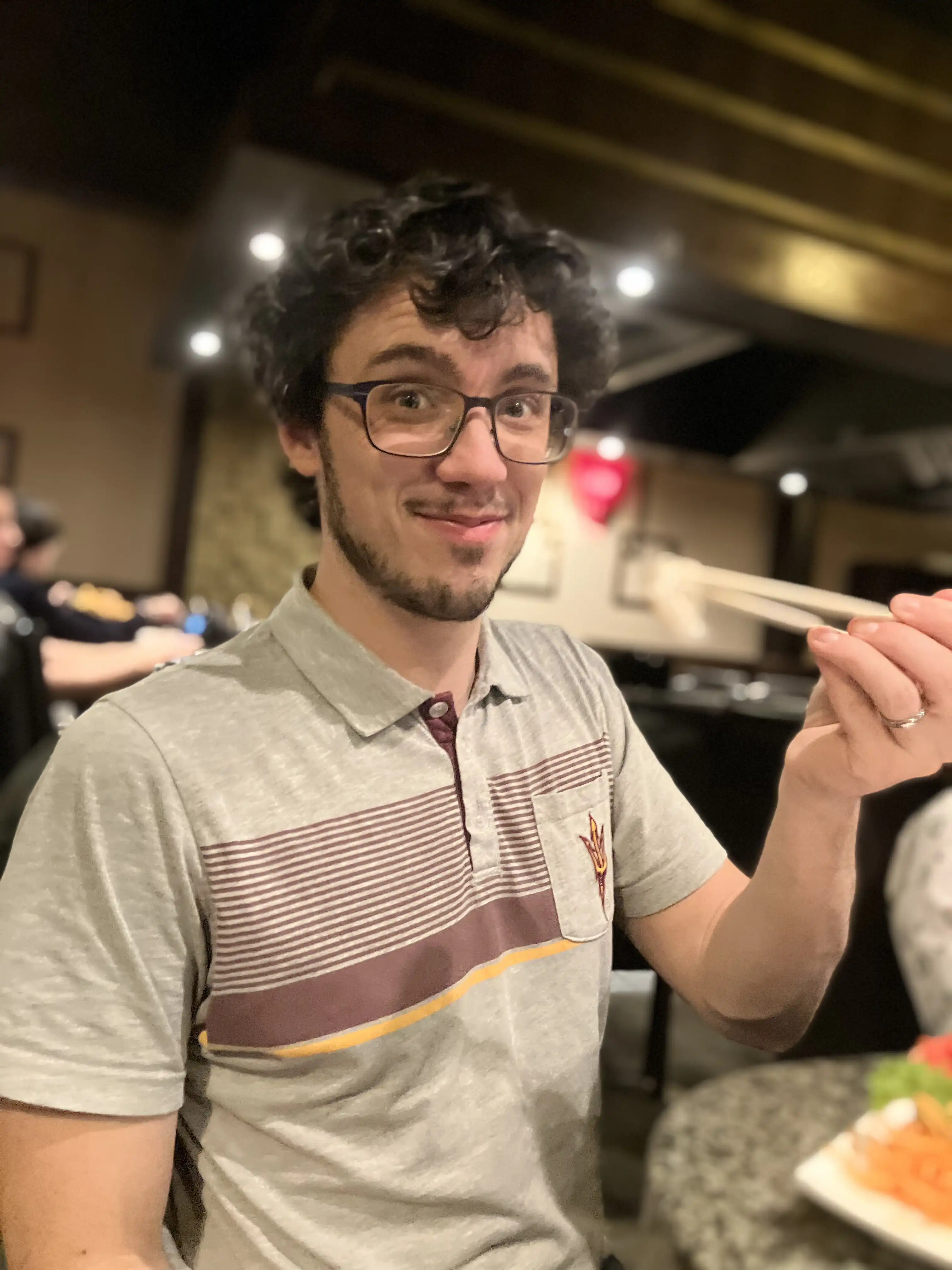 Alex holding up chopsticks with a smile on his face