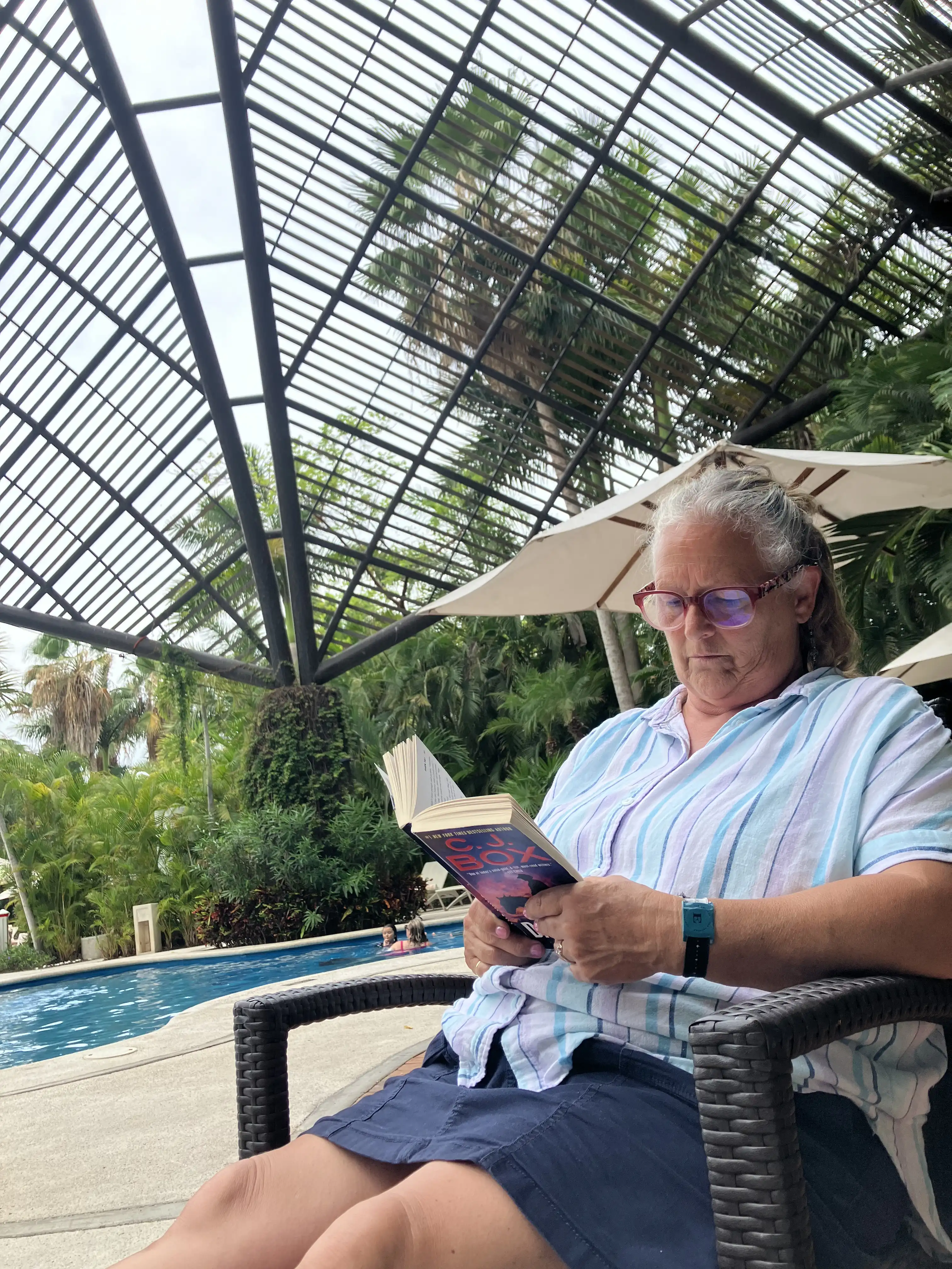 Jaynne lounging by the pool, reading her novel.